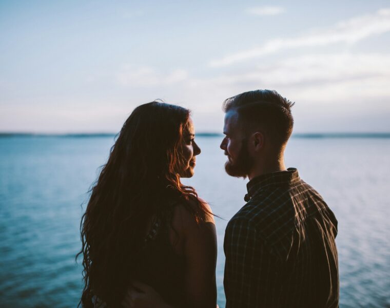 man and woman standing while looking each other near body of water